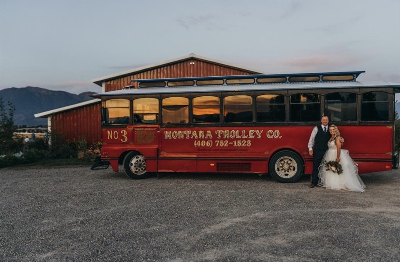 Bride and groom beside Ruby No. 3 at dusk near a red barn